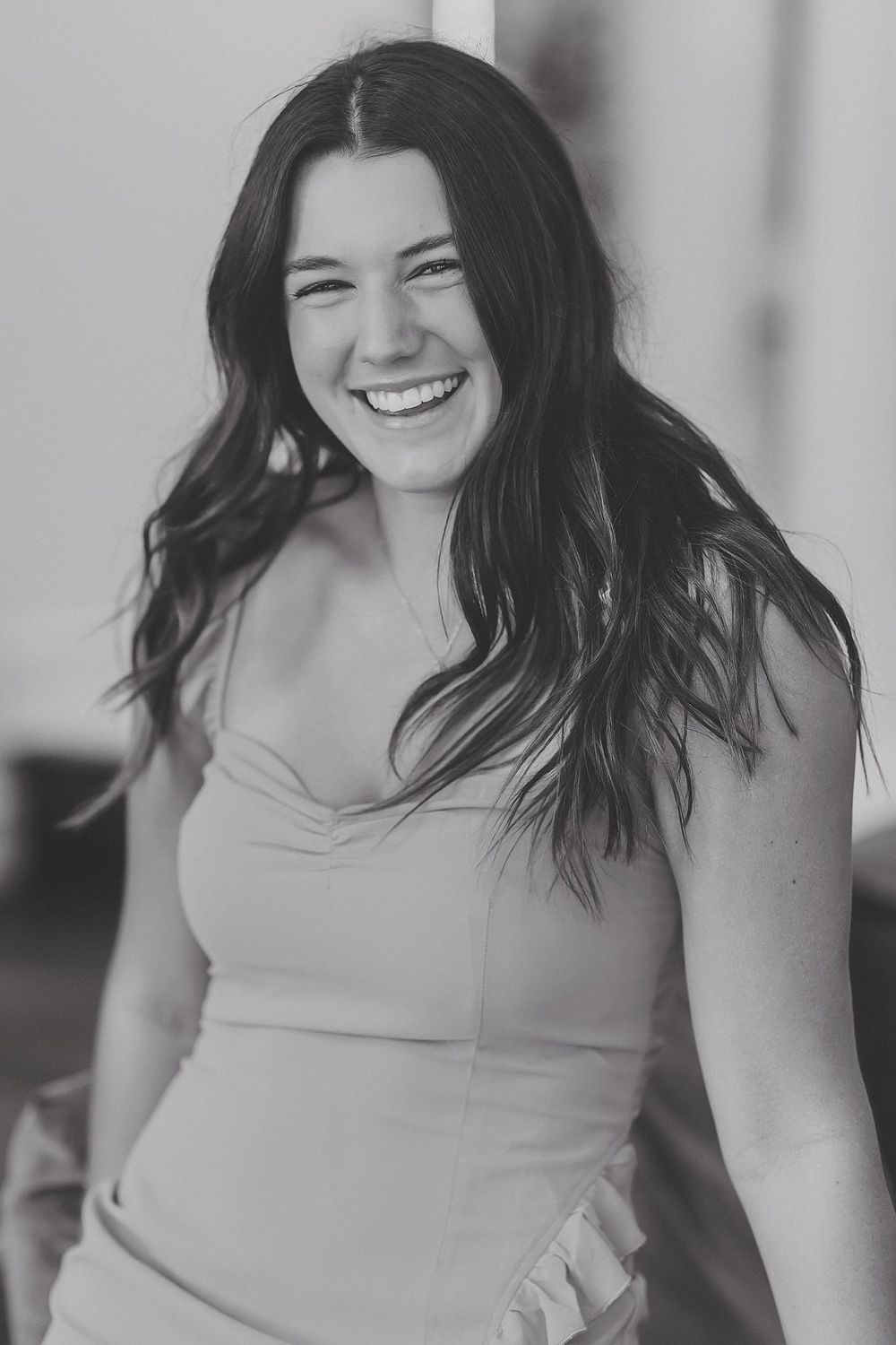 A candid black and white portrait of a woman laughing with flowing dark hair.