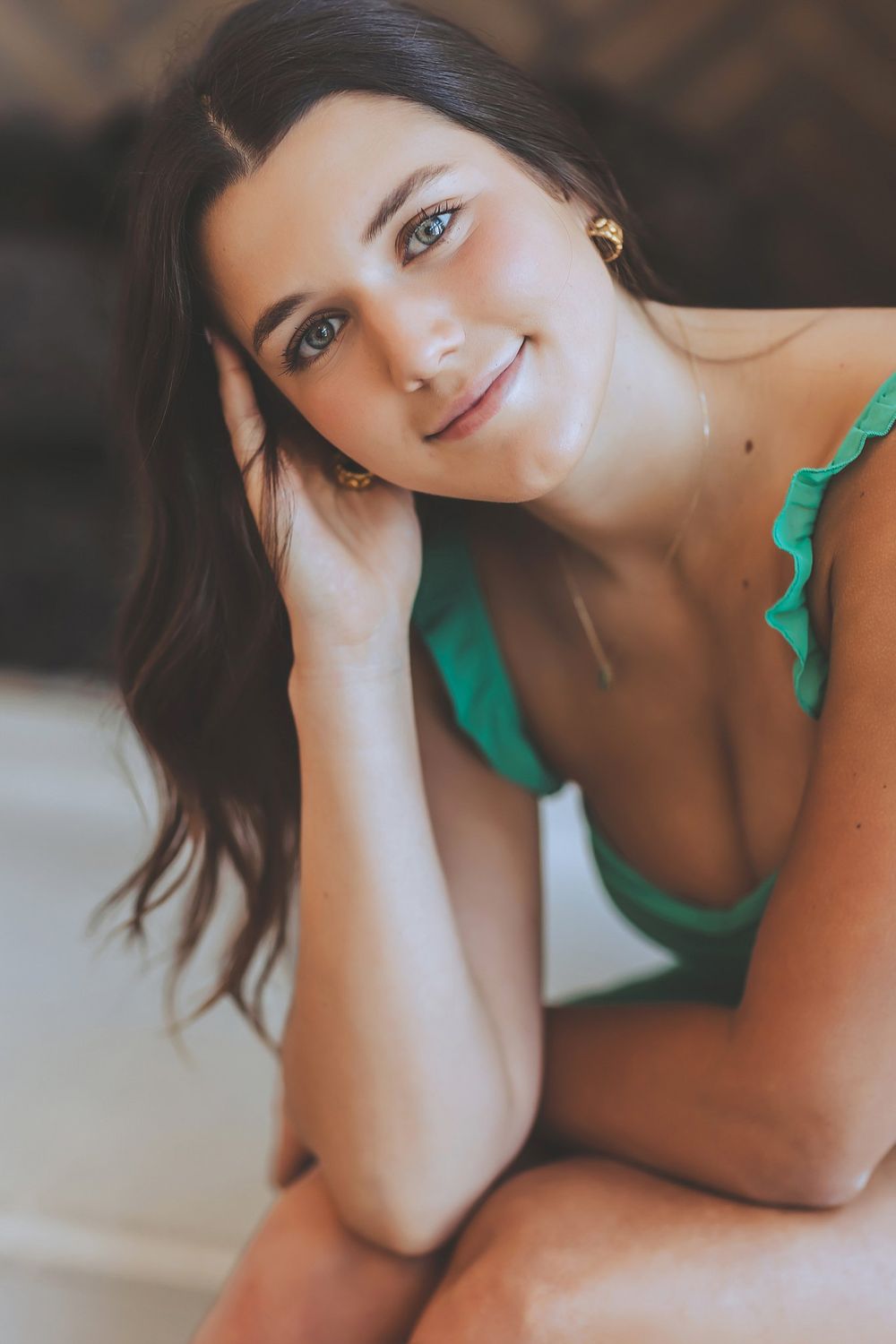 A woman in green lounging and smiling while resting her head on her hand.