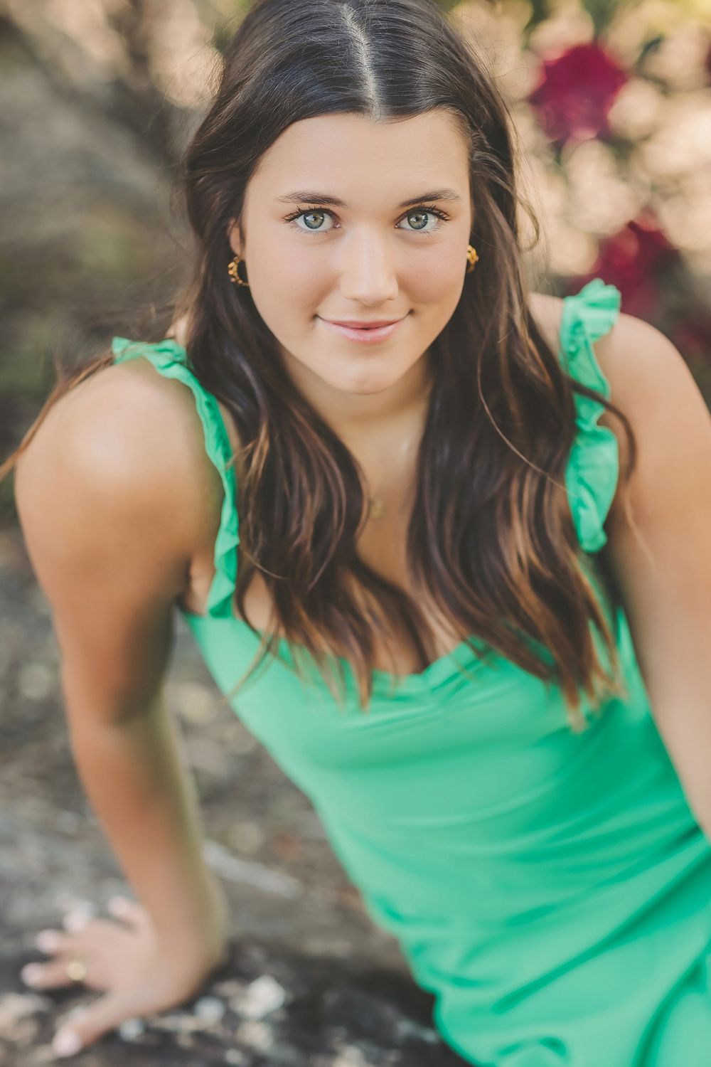 A woman in a green summer dress poses outdoors against a floral background.