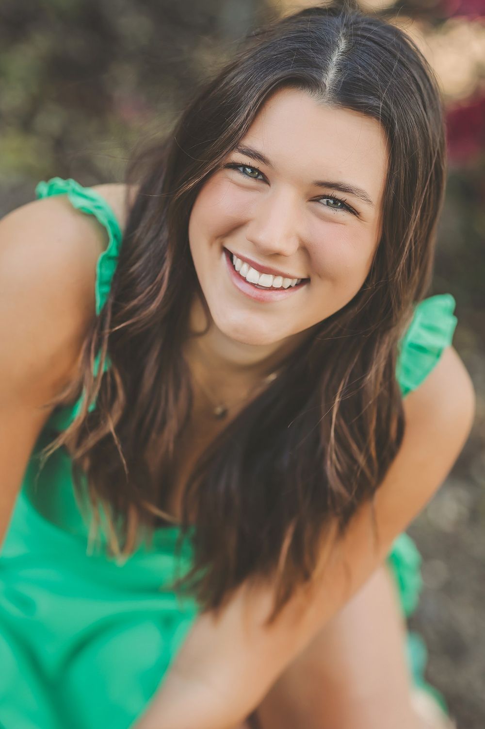 Close-up outdoor portrait of a woman in green with a bright genuine smile.