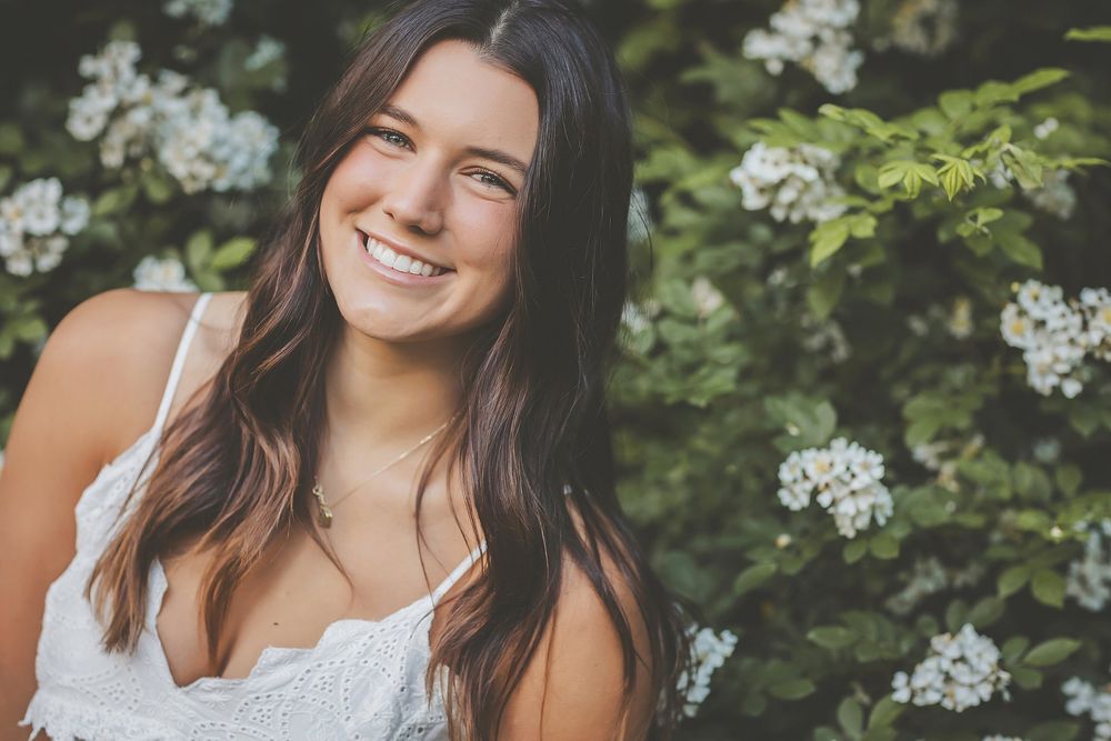 A natural outdoor portrait featuring white flowers and greenery in the background.