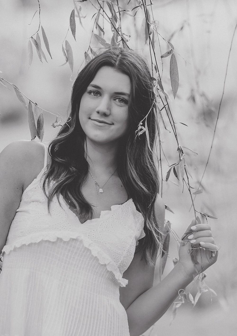 Black and white portrait showing a gentle smile and flowing hair in a natural outdoor setting.