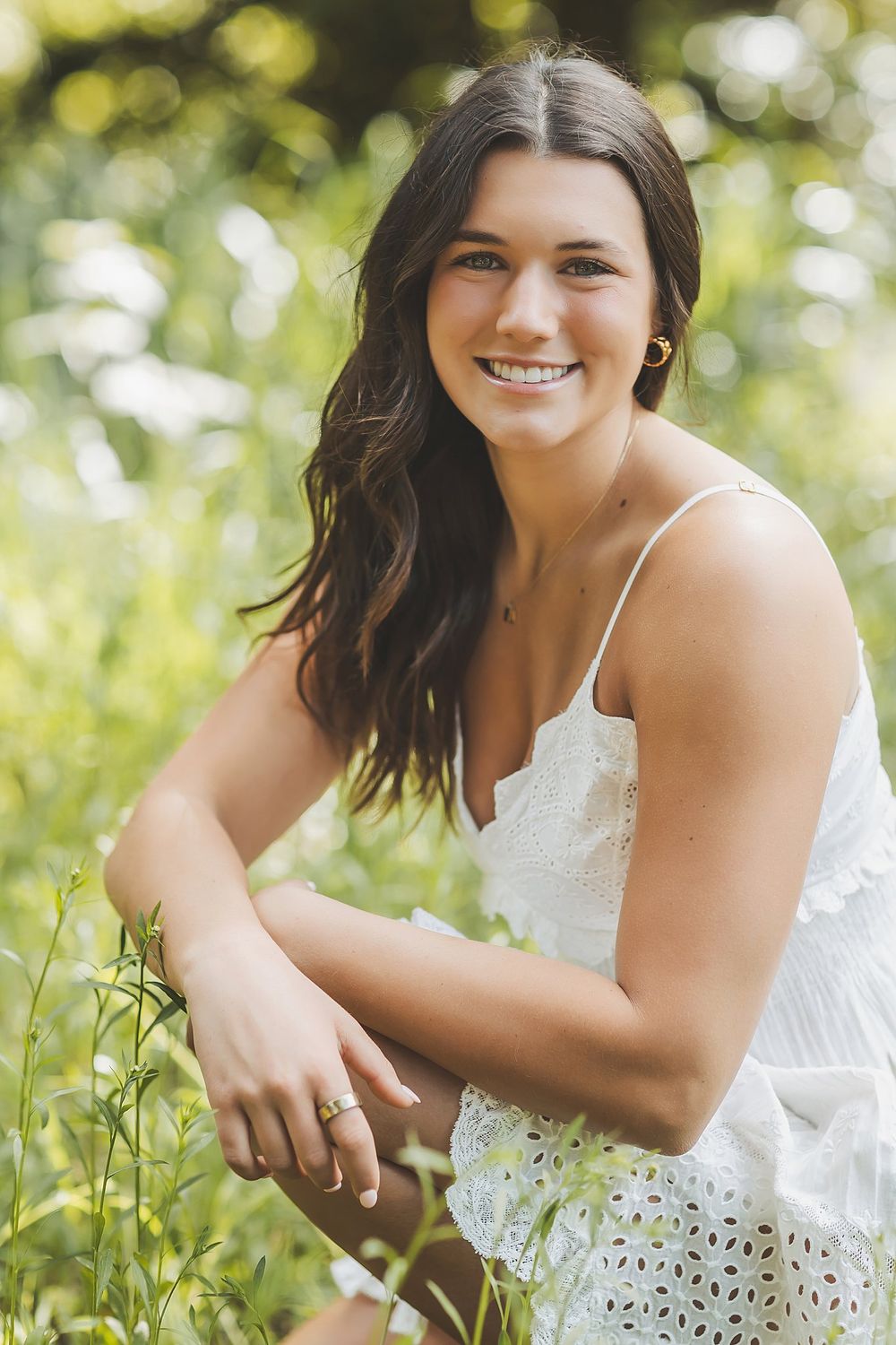 Playful outdoor portraits in white dress amid green summer foliage.