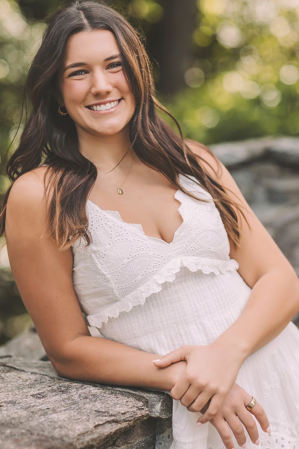 Close up portrait showing a white lace sundress and delicate necklace against natural bokeh background.