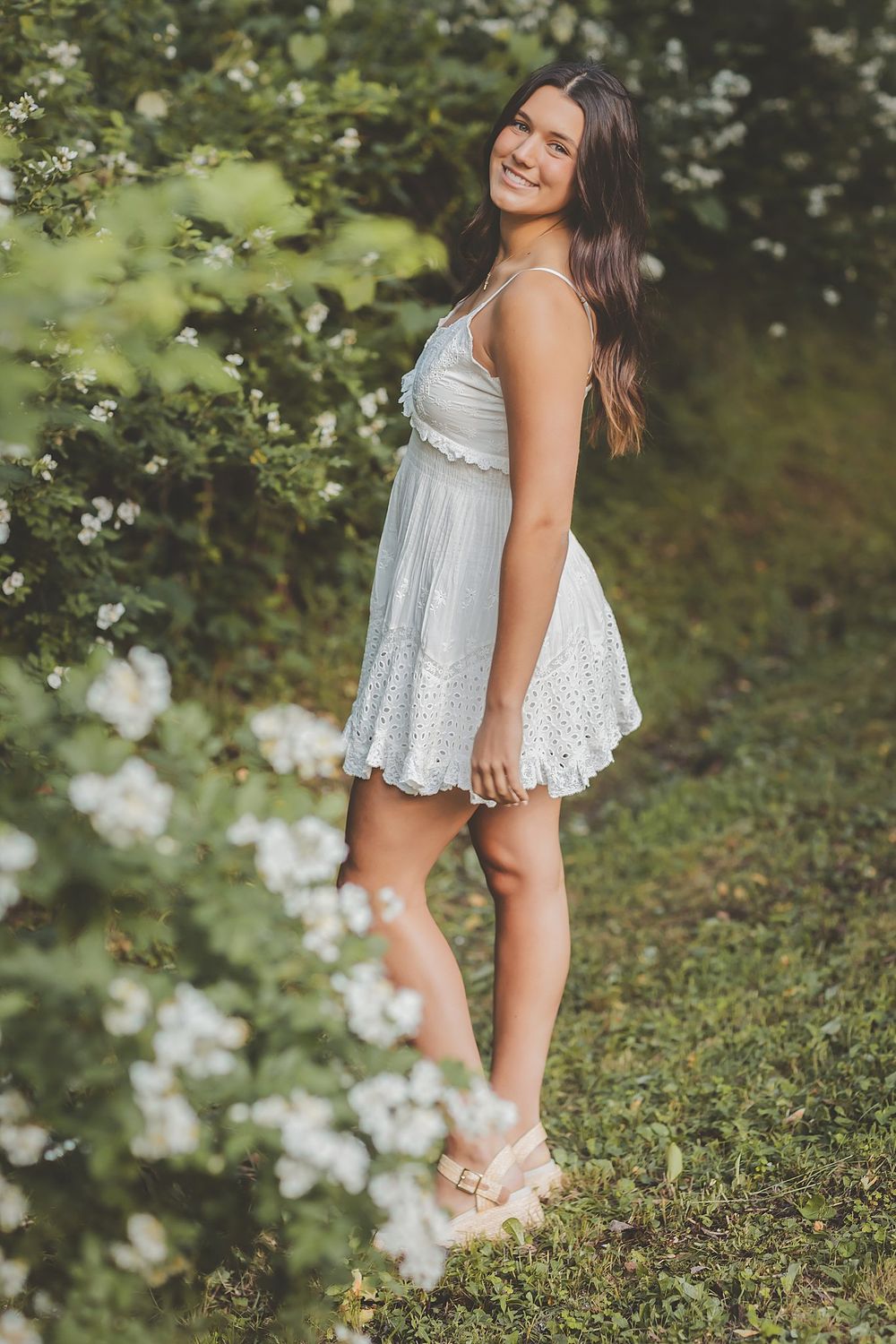 A dreamy garden portrait features a white lace dress among blooming flowers and greenery.