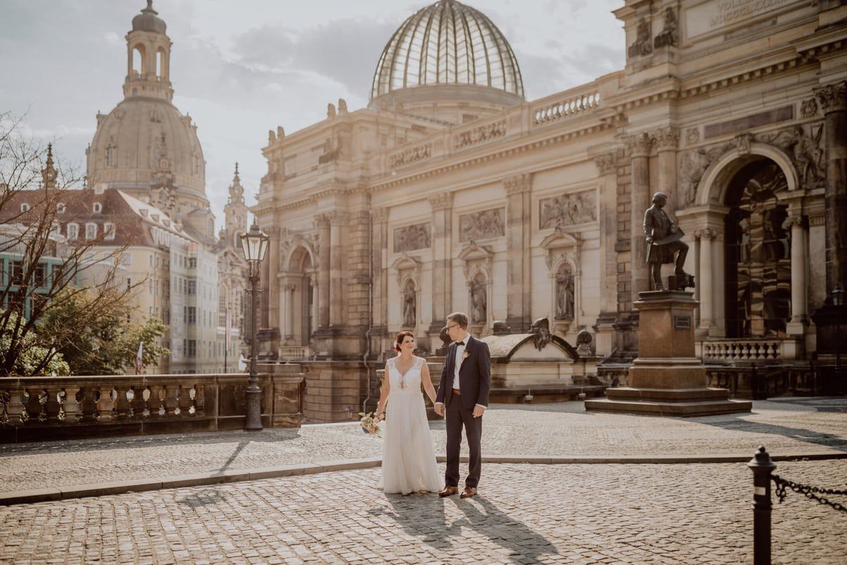 A couple standing in front of the historic Dresden Academy of Fine Arts building on a sunny day.