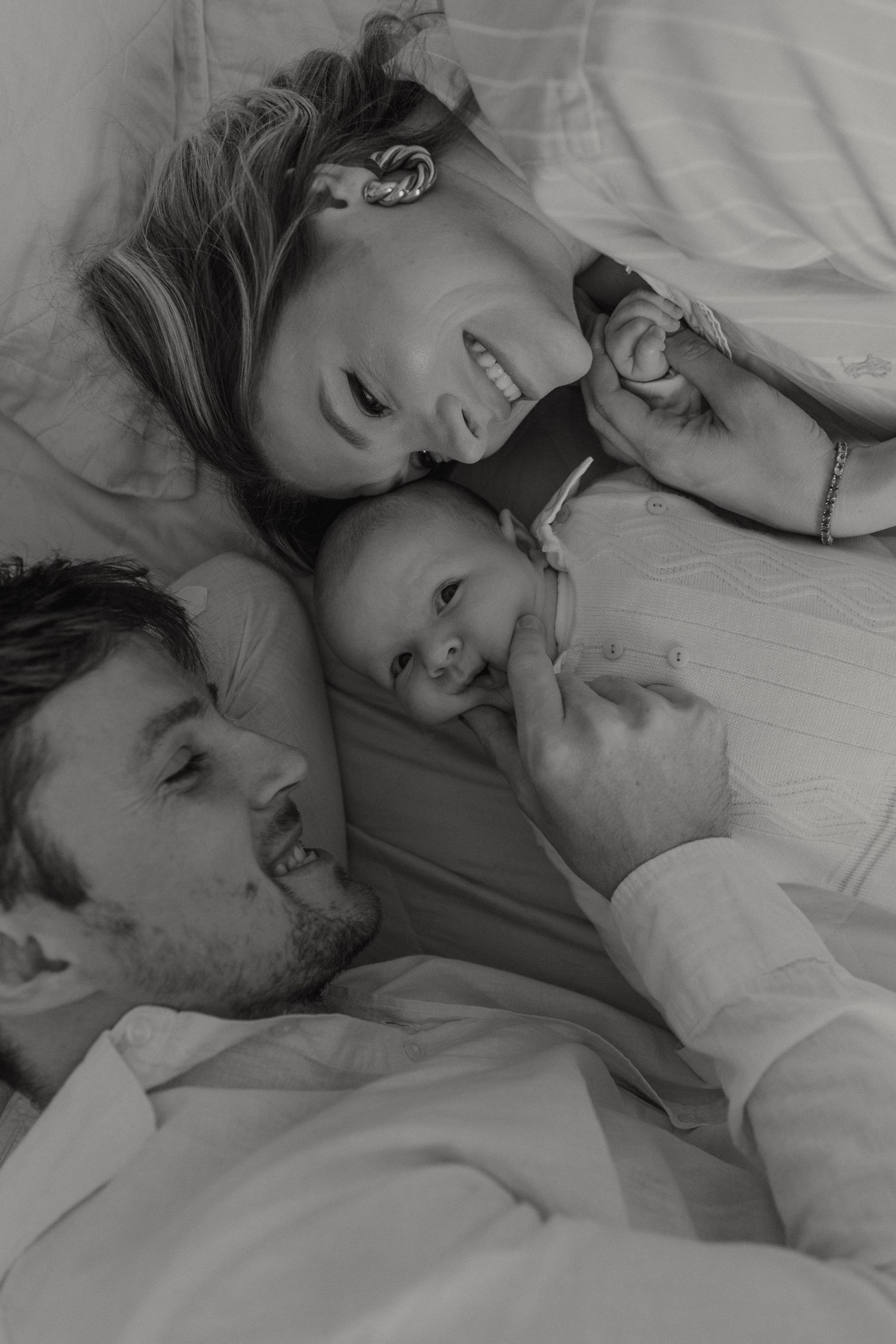 A tender black and white family moment with parents and baby lying together.