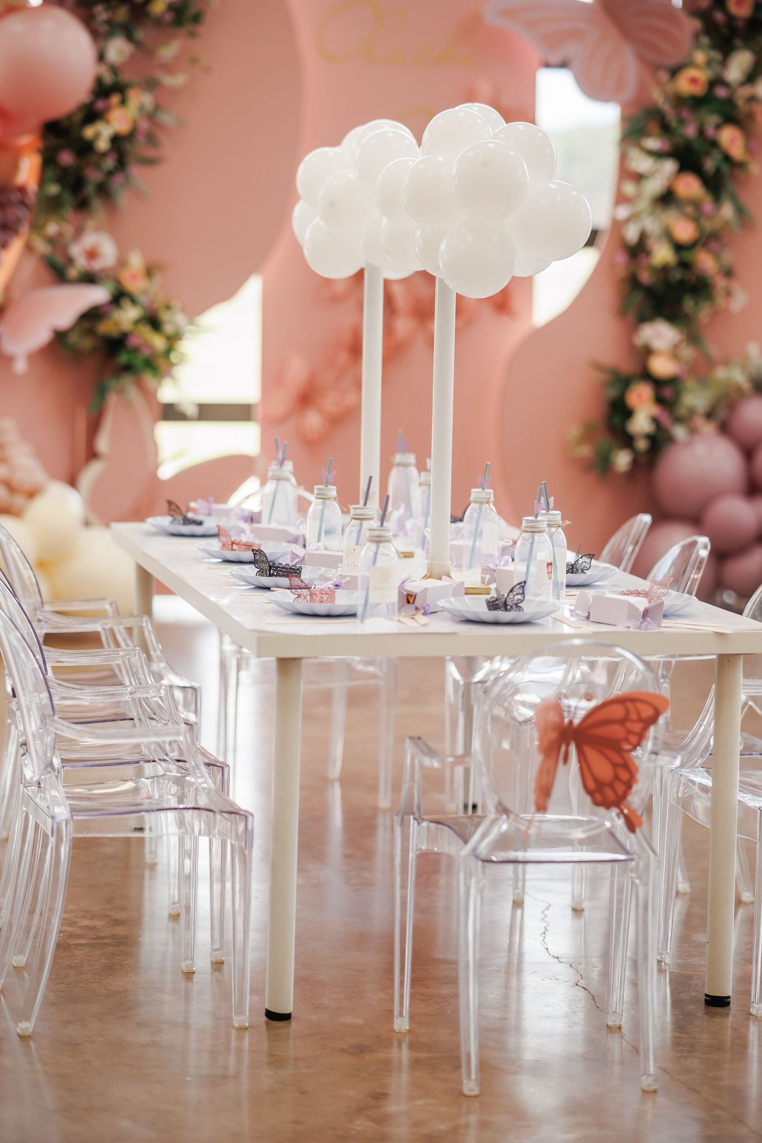 Bella Cavalli birthday party decor with transparent ghost chairs and pink walls decorated with balloon and floral arrangements.