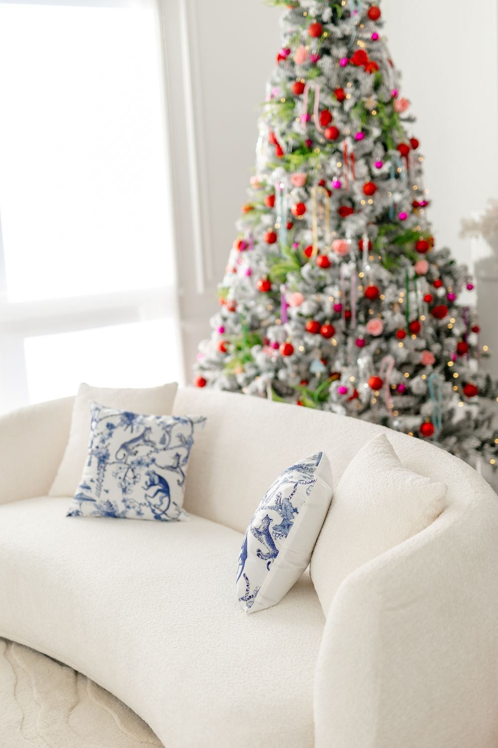 Elegant white curved sofa with blue patterned pillows next to a decorated Christmas tree with red and white ornaments.
