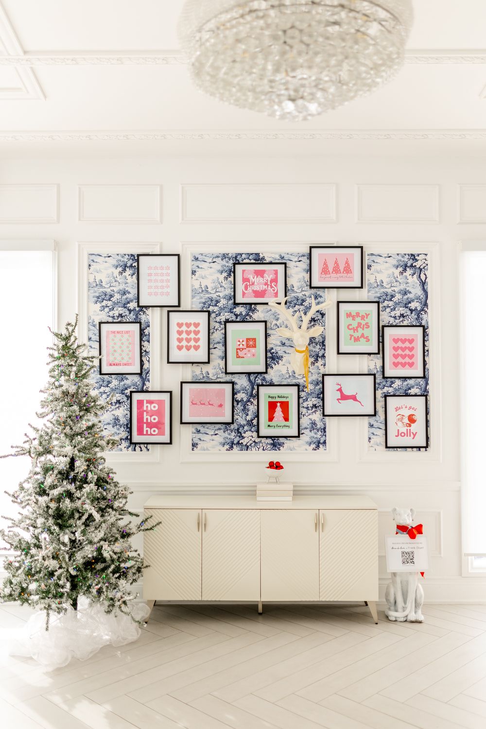Bright white room with Christmas decorations featuring multiple framed art prints and a flocked Christmas tree against wall.