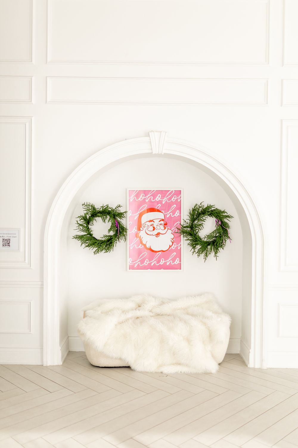 Light and airy Christmas interior with white paneled walls, green holiday wreaths, and pink artwork in an arched alcove.