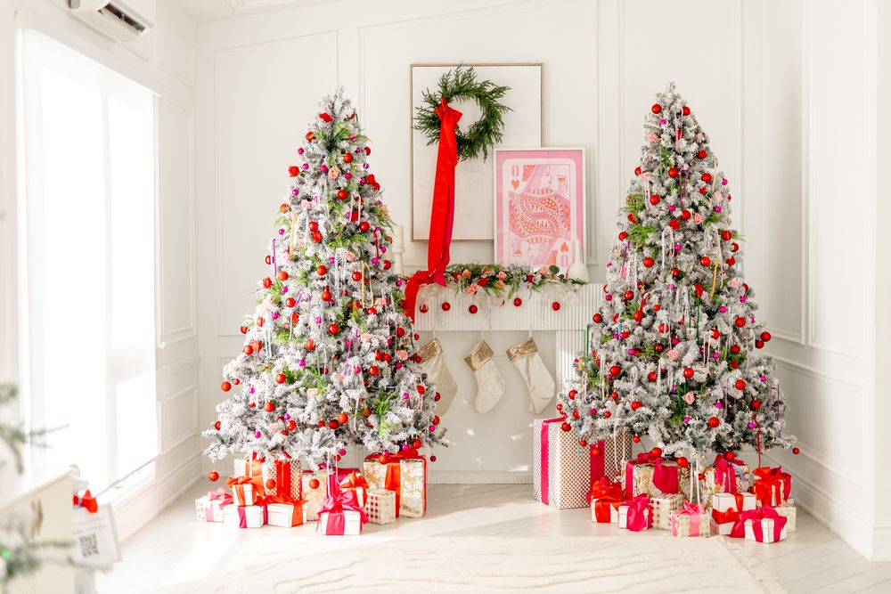 White Christmas living room with elegant flocked trees and red and white wrapped presents under each tree.