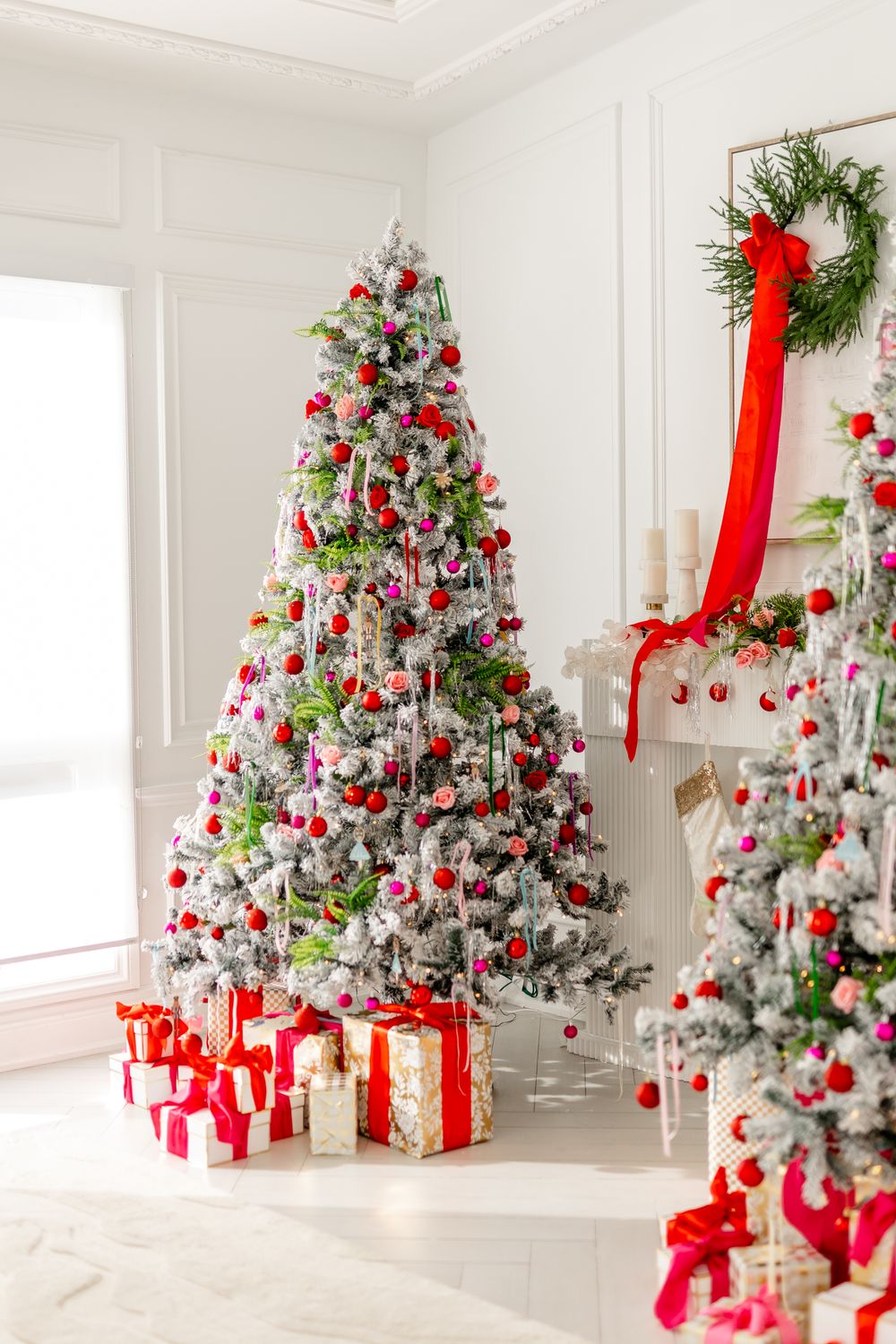 A white flocked Christmas tree decorated with red ribbons and ornaments with wrapped presents underneath.