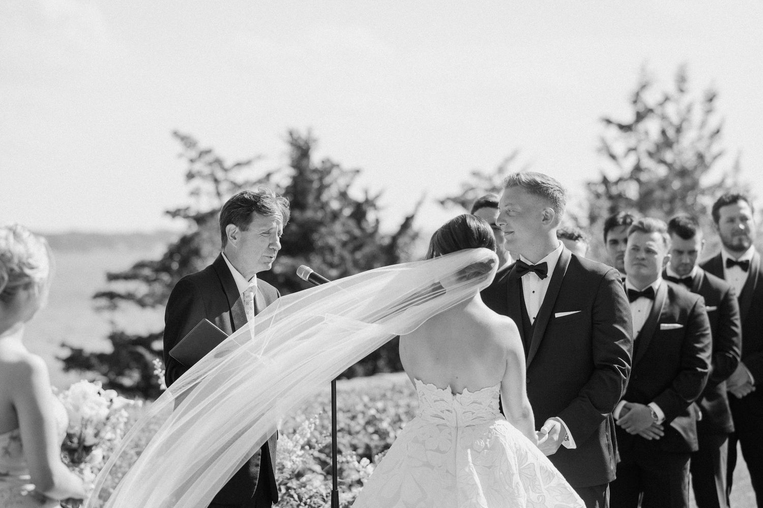 Wedding ceremony guests seated outdoors on a sunny day with white chairs.