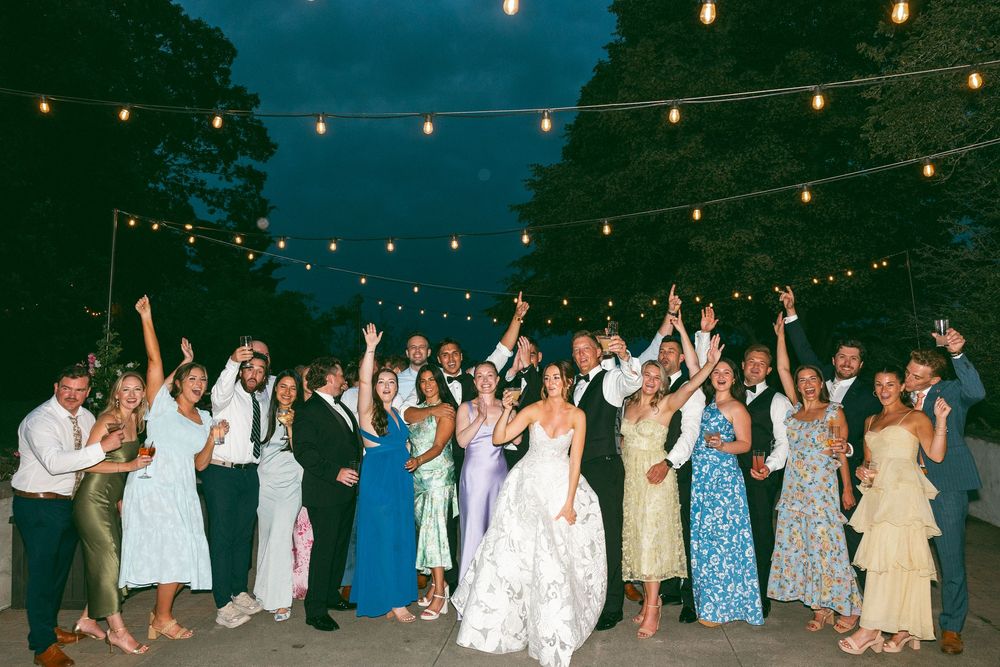 Wedding guests dancing outdoors under string lights at night.