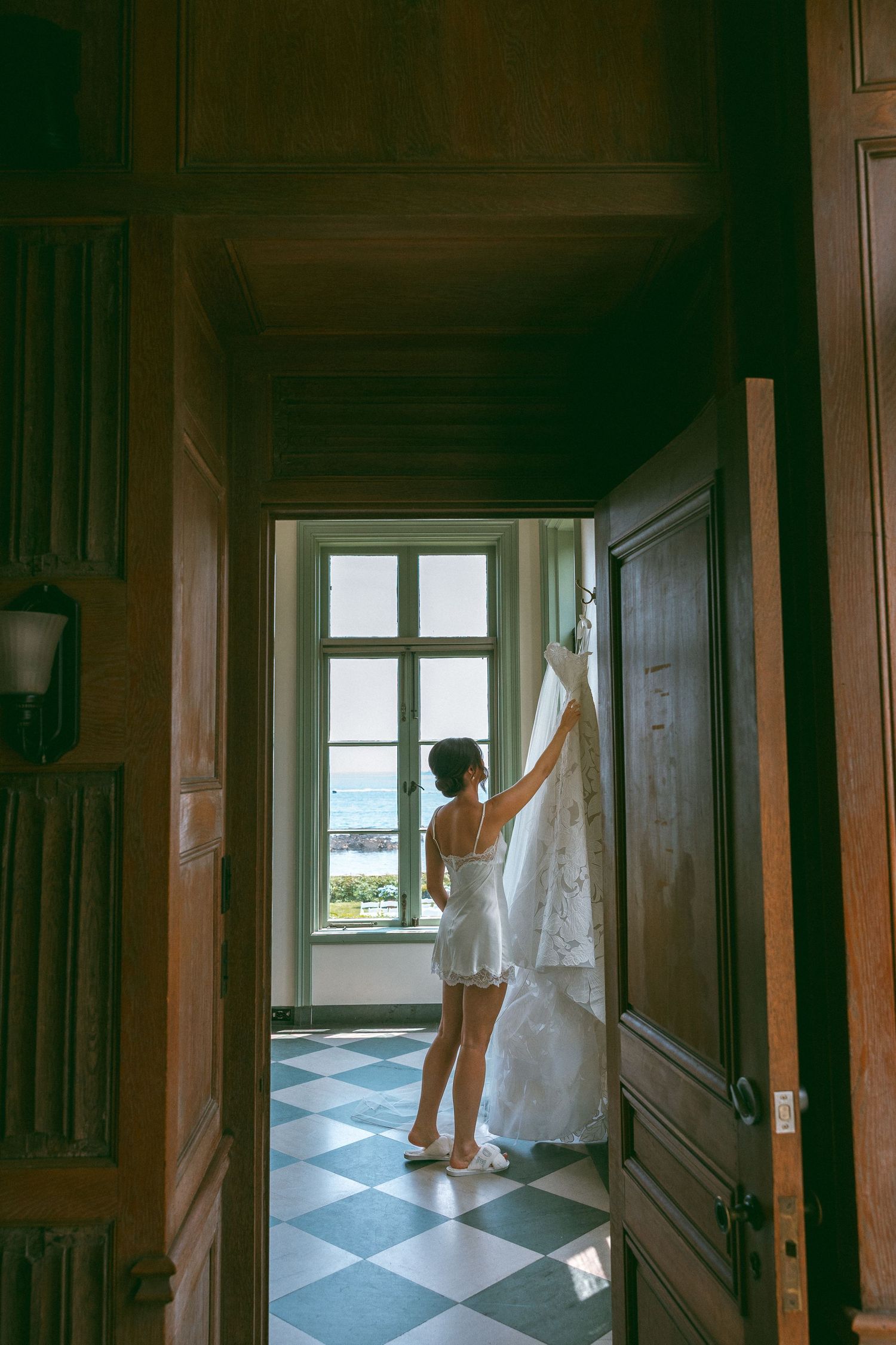 Silhouetted figure reaching for wedding dress in room with checkered floor.