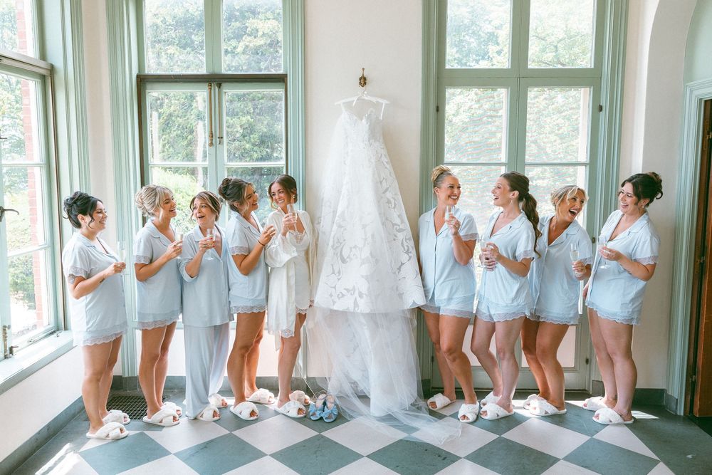 Bridesmaids in light blue dresses react emotionally while viewing a wedding dress reveal.