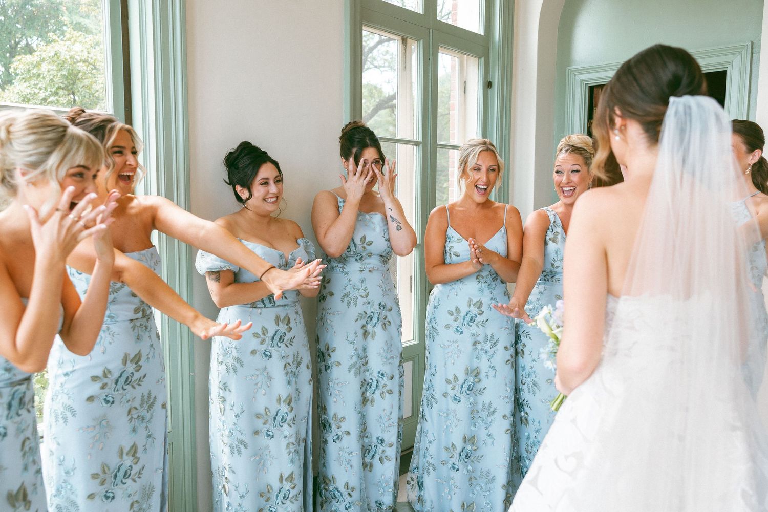 Wedding party wearing pale blue floral bridesmaid dresses share an emotional moment.