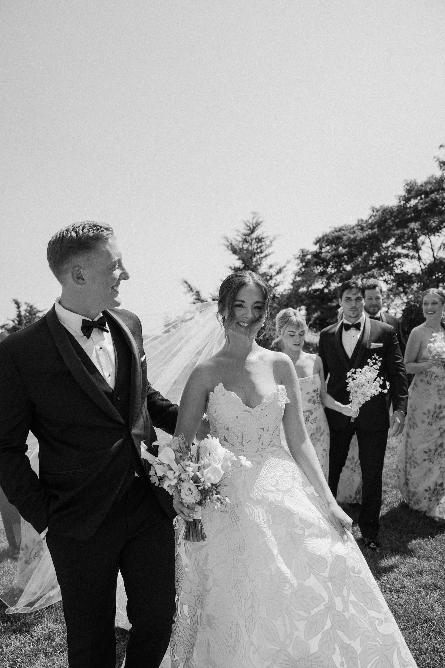 Black and white photo of a wedding party celebrating outdoors on a sunny day.