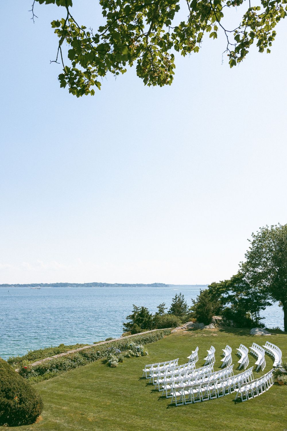 White wedding chairs arranged in curved rows on a scenic oceanfront lawn.