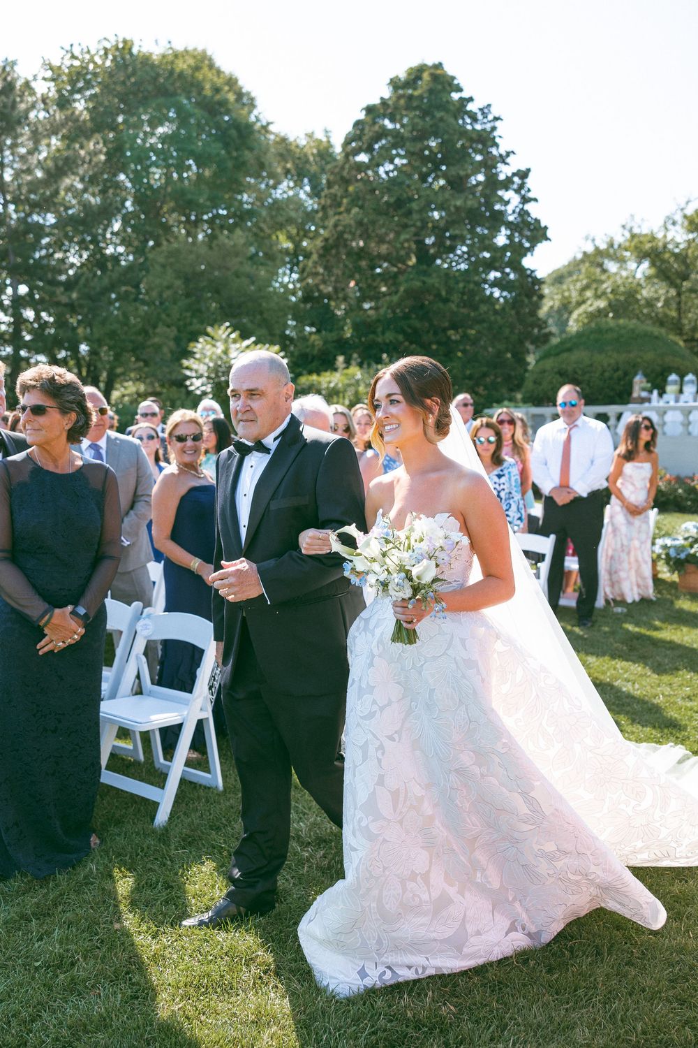 Wedding guests gather on a grassy lawn during an outdoor summer ceremony.