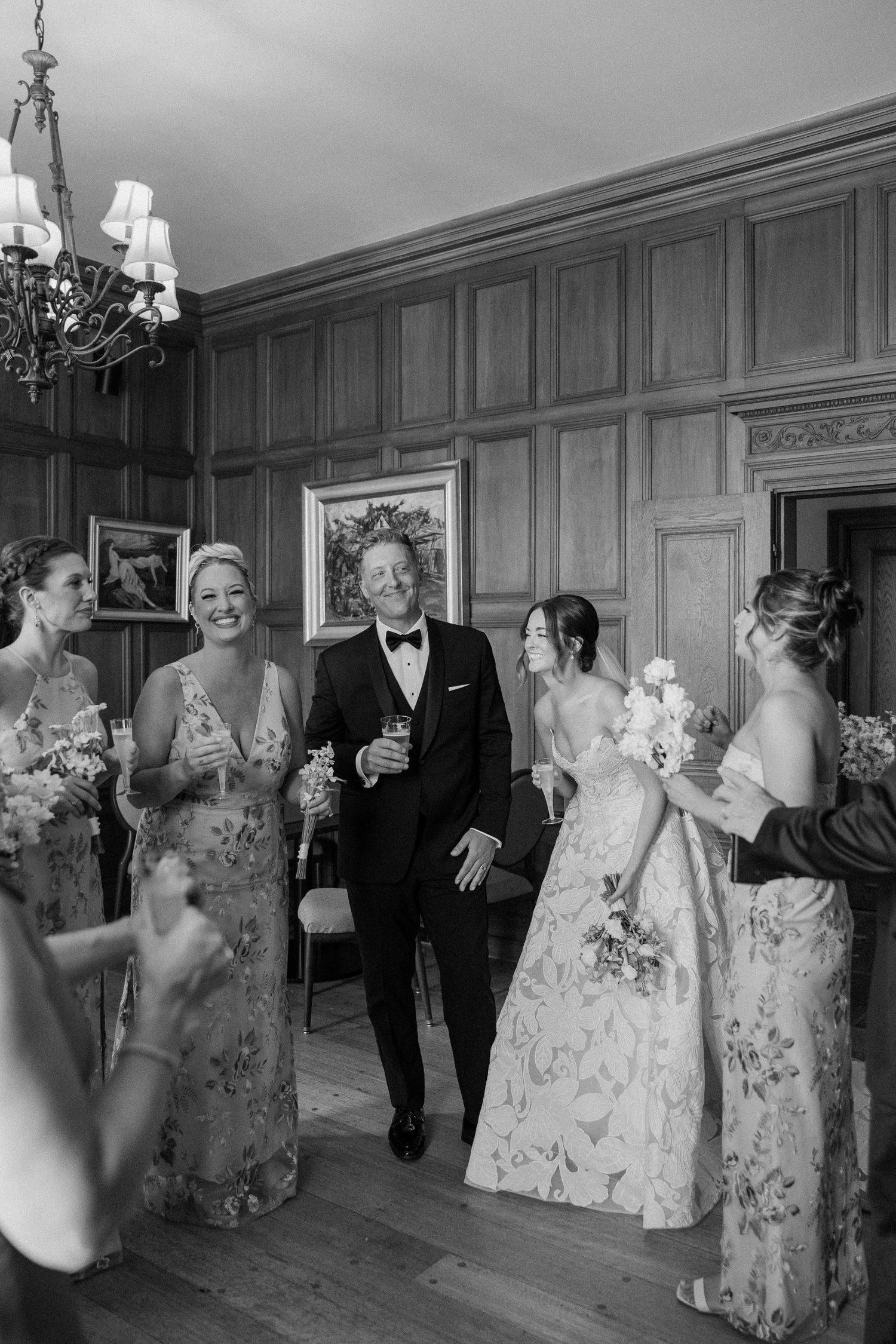 Wedding party dancing and celebrating in an elegant wood-paneled ballroom during reception.