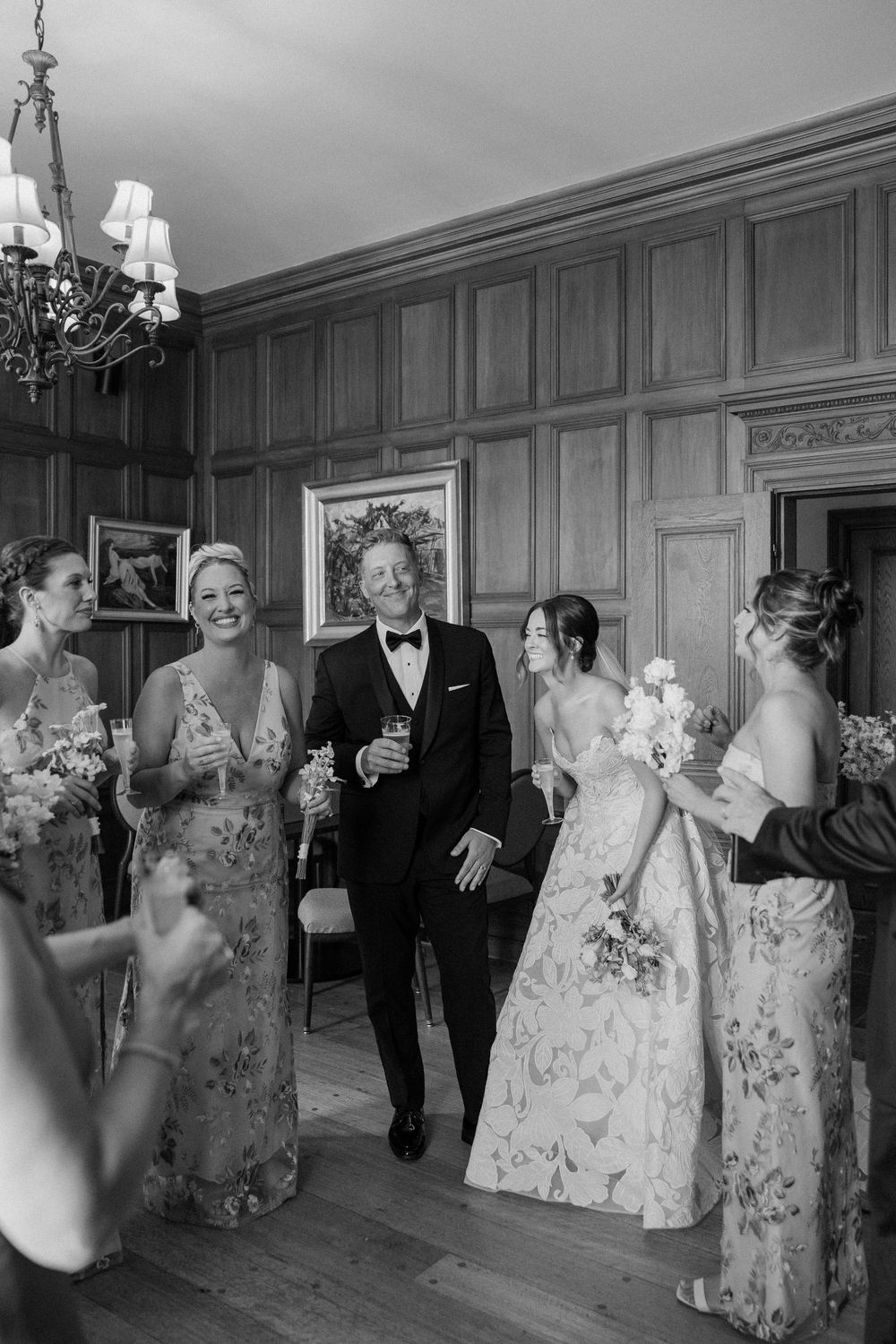 Wedding party dancing and celebrating in an elegant wood-paneled ballroom during reception.