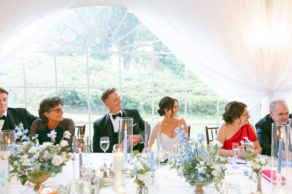 Reception dinner setup under an elegant white tent with floral centerpieces.