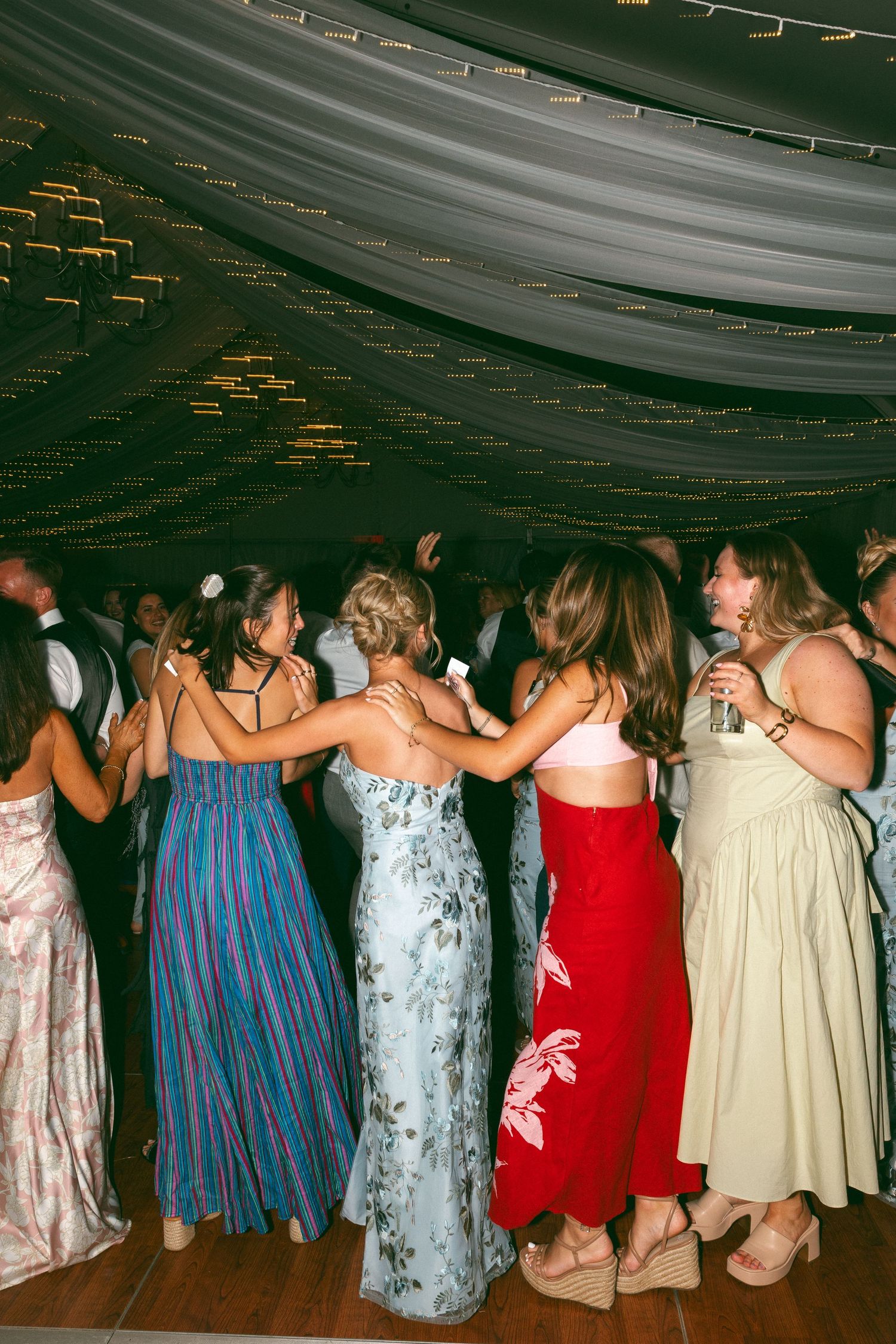 Wedding guests dancing together in formal dresses under draped fabric ceiling.