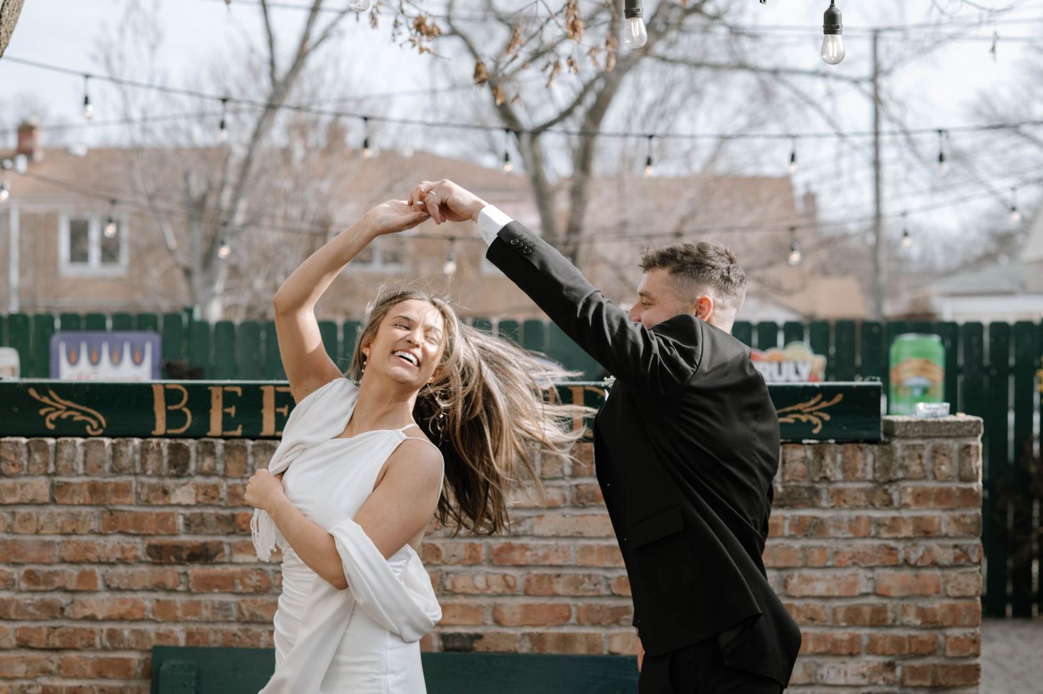 Two people dance and spin together joyfully in a walled outdoor courtyard on a cloudy winter day.