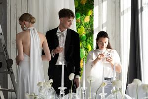 People in formal attire gather around an elegantly set dining table with wine glasses and candlesticks.