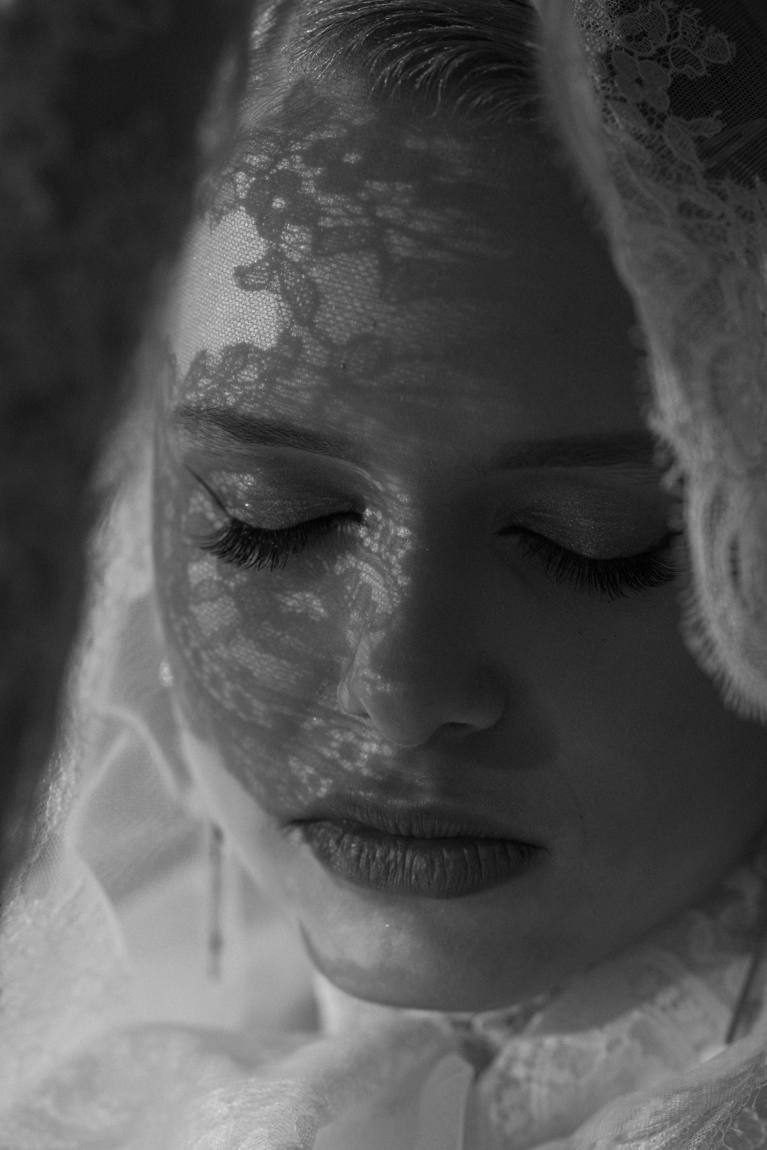Artistic black and white portrait with delicate lace shadows casting patterns across closed eyes and serene expression.