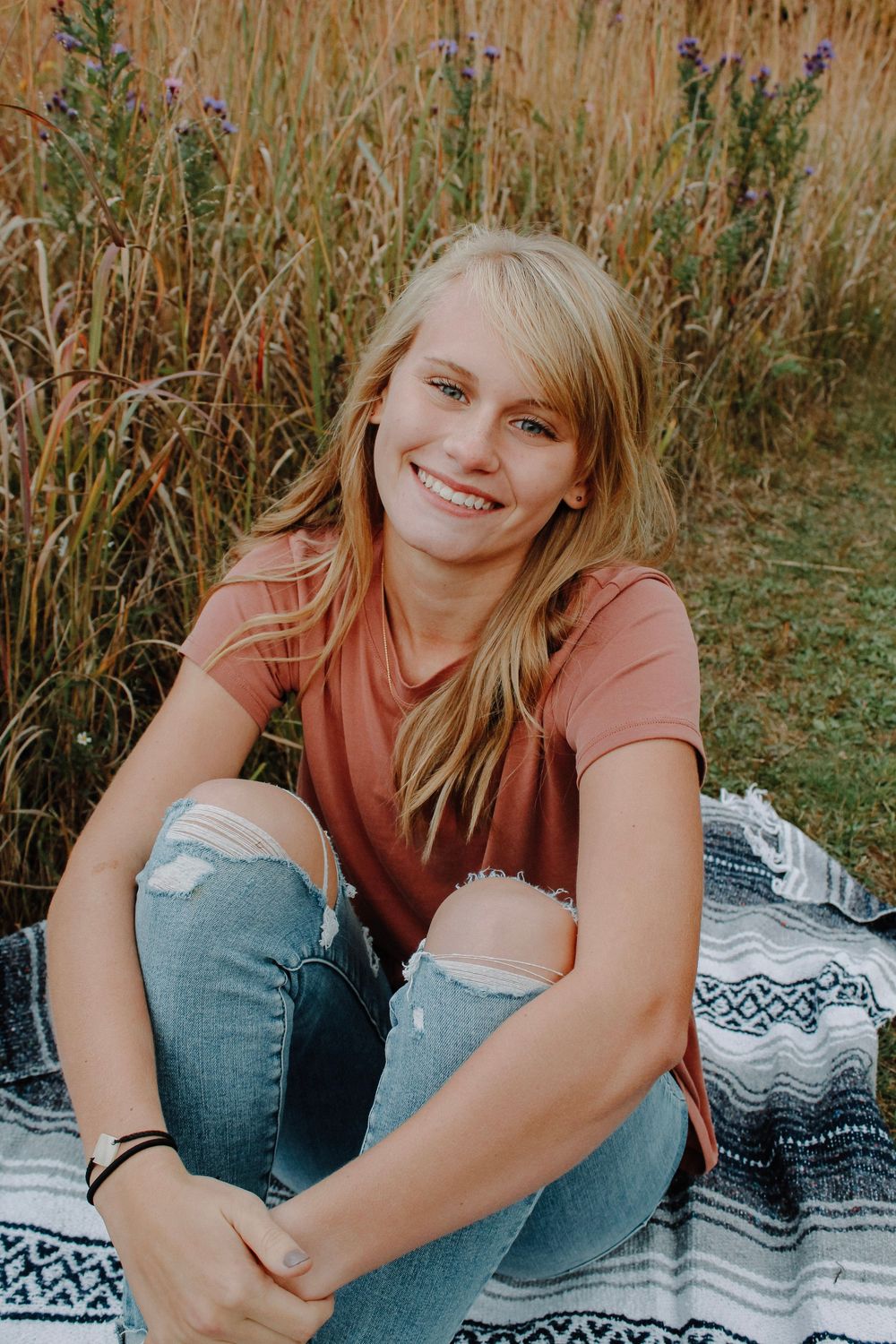 Senior girl in a field on a blanket during golden hour.