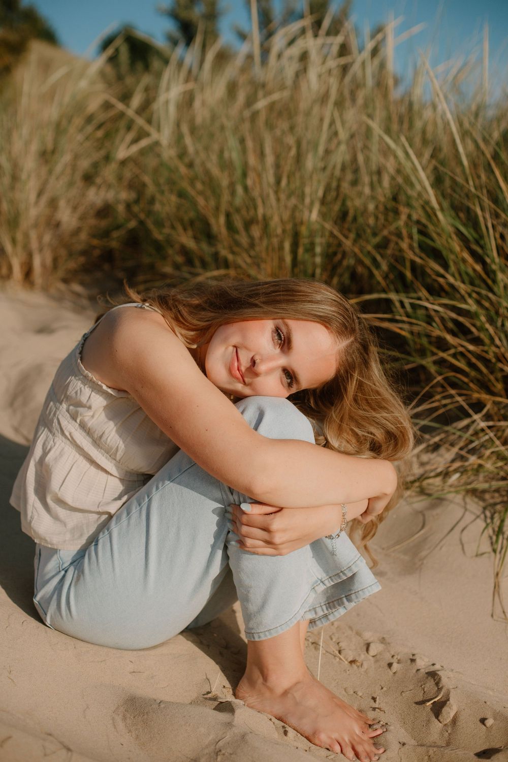 Senior girl sitting in sand at a beach sunset photo session in Holland, MI.