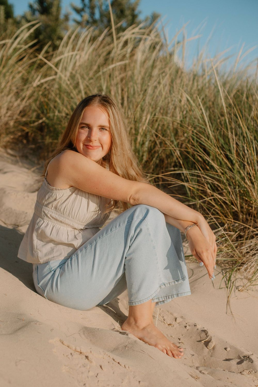 Senior girl sitting in sand at a beach sunset photo session in Holland, MI.