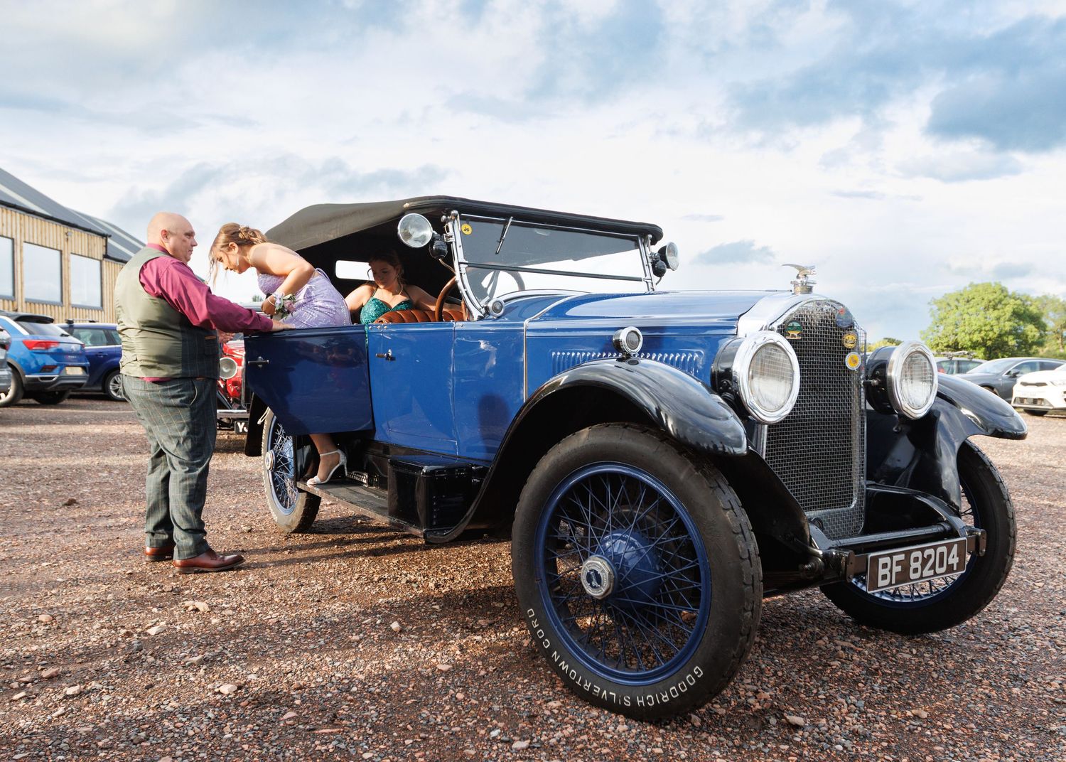 A vintage blue classic car on display with people gathered around to admire it.