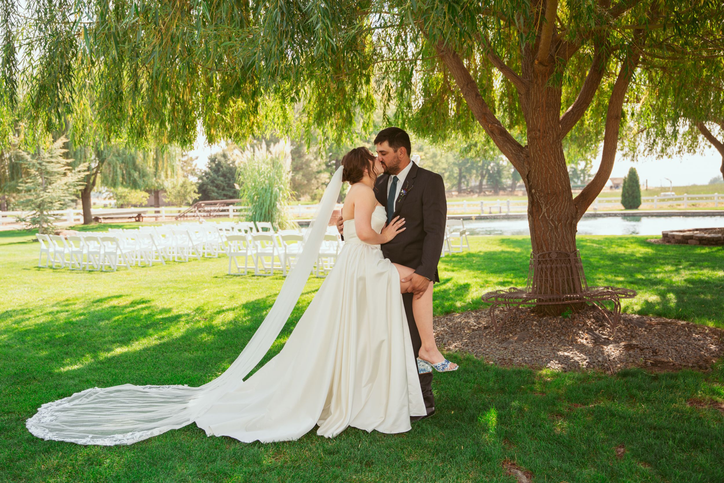 A romantic moment captured under a weeping willow tree during an outdoor wedding ceremony.