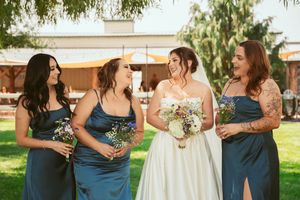 Bridesmaids in navy blue dresses carrying small floral bouquets enjoy an outdoor garden wedding celebration.
