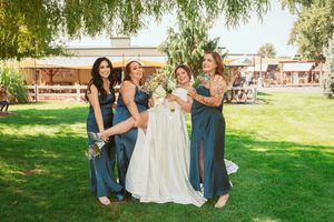 Bridal party in blue dresses laughs together on sunny lawn at outdoor wedding venue.