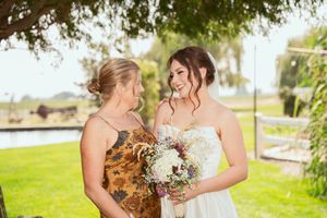 Two people in wedding attire share a joyful moment outdoors with one holding a beautiful floral bouquet.