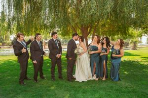 Wedding party poses together under elegant drooping willow trees in an outdoor garden setting.