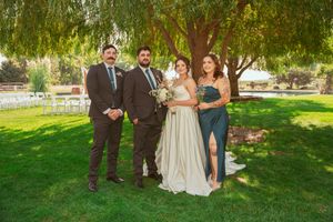 A small wedding party poses together on a sunny lawn beneath a drooping willow tree.