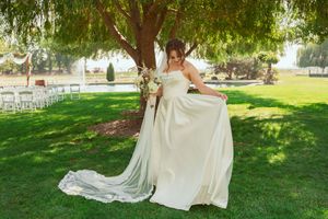 A bride in a flowing white gown twirls on a grassy lawn with white chairs set up for an outdoor wedding ceremony.