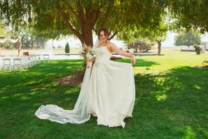 Someone in a flowing white wedding dress poses elegantly on a green lawn with outdoor ceremony seating visible.