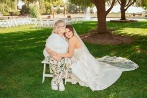 A touching outdoor wedding moment on a grassy lawn beneath a tree, with a white lace gown and chair.