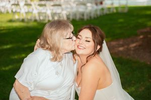A couple embraces during an outdoor wedding photoshoot with white dress details and a scenic natural backdrop.