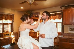 A couple shares a playful cake-feeding moment during their wedding celebration in a rustic indoor setting.