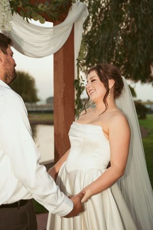 A joyful couple shares a tender moment during their outdoor wedding ceremony under a decorated gazebo.