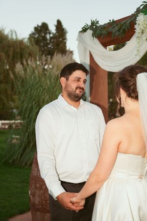 A couple in wedding attire shares an intimate moment while sitting together outdoors at sunset.