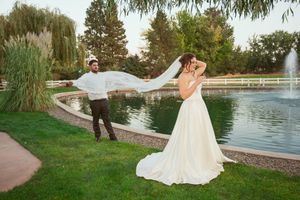 A playful wedding photo by a pond with fountain where a couple strikes dramatic poses.
